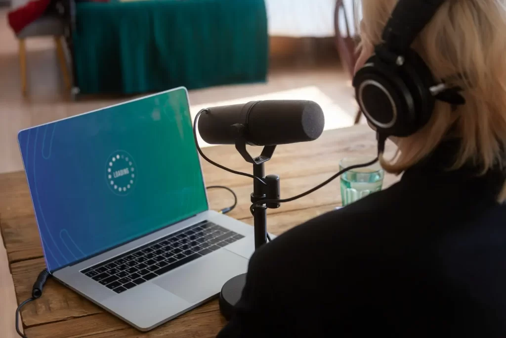 Mulher hospeda episódios com um microfone profissional e notebook, ilustrando onde hospedar podcast.