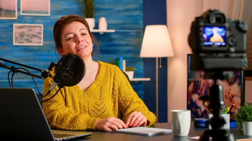 Mulher gravando vídeo com câmera no tripé em um estúdio para divulgar podcast